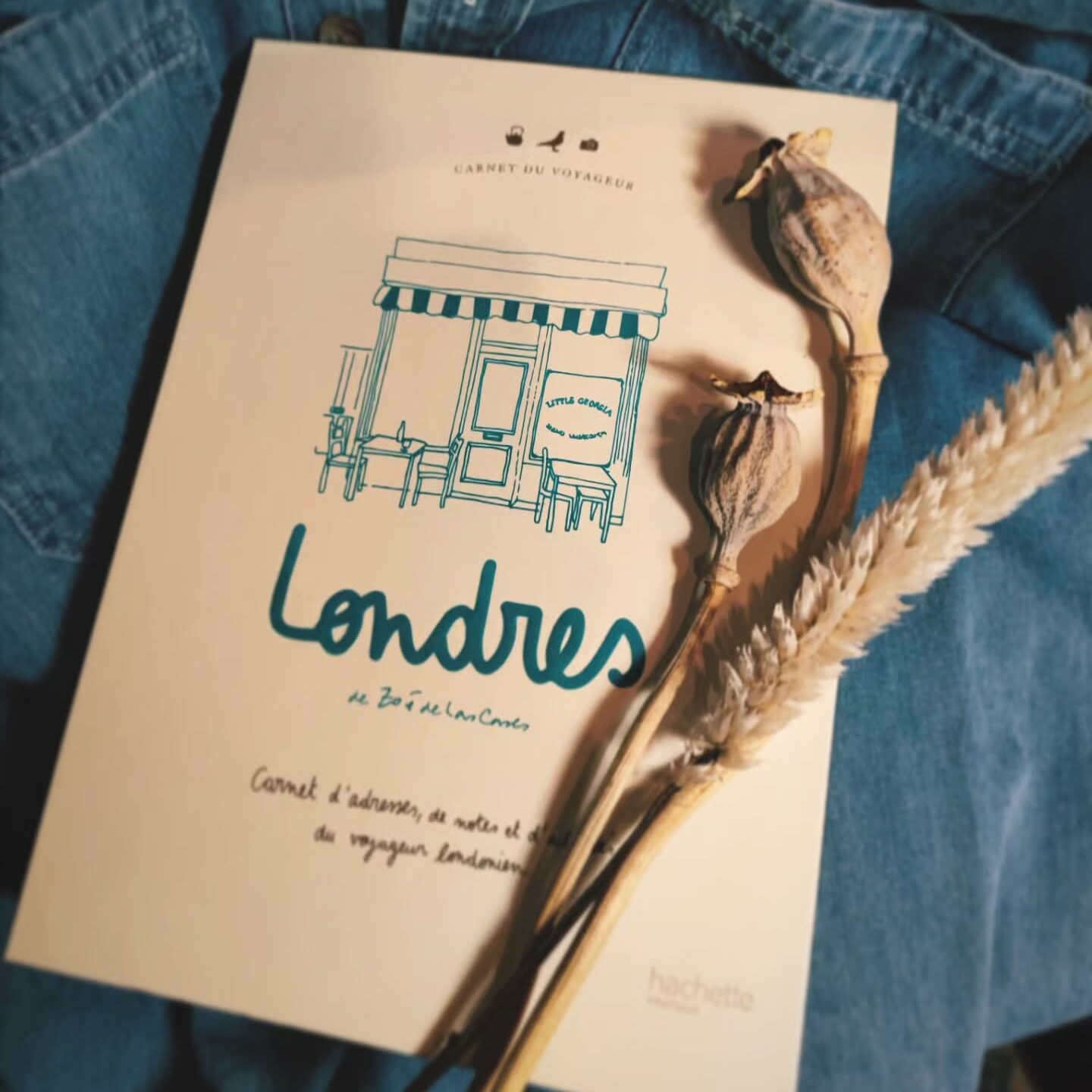Carnet de voyage "Londres" posé sur une veste en jean avec des fleurs séchées