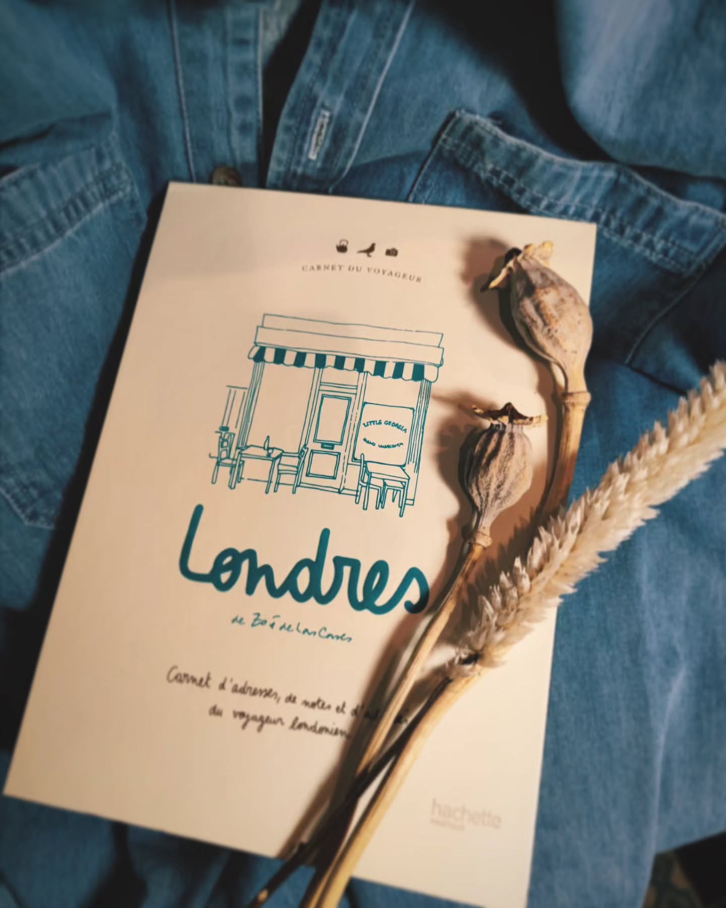 Carnet de voyage "Londres" posé sur une veste en jean avec des fleurs séchées